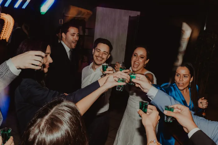 Noivos e convidados a brindar com copos de shot no meio da pista.